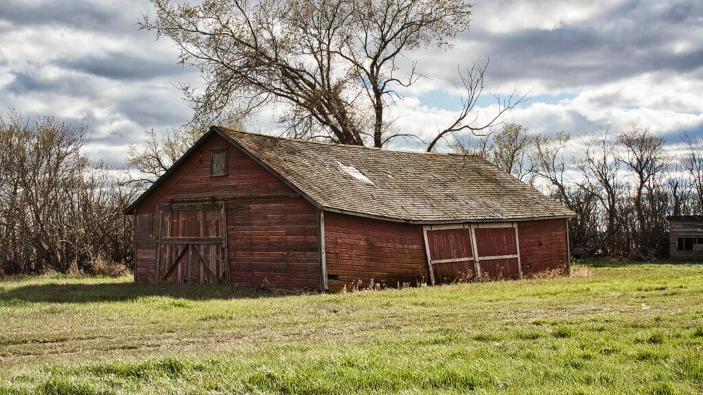 A weathered red barn stands in an autumn countryside setting under a cloudy sky.